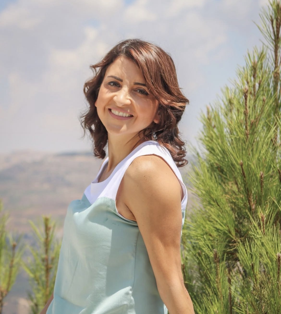 Dr. Jomana Elaridi smiling outdoors beside pine trees